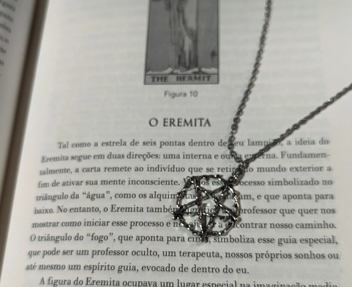 Colar pentagrama místico gótico com corrente de aço inox e pingente de liga metálica sobre a página do livro O Eremita.
