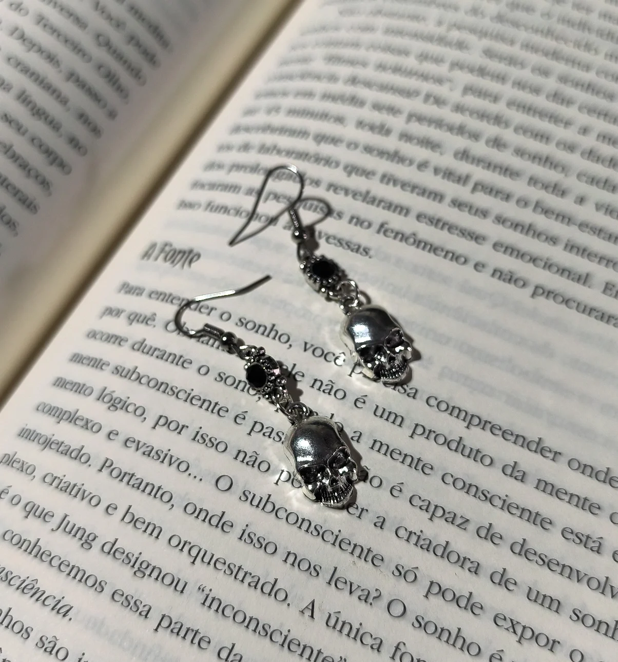 Brinco caveira gota preta gótico em liga metálica prateada com strass preto sobre as páginas de um livro.