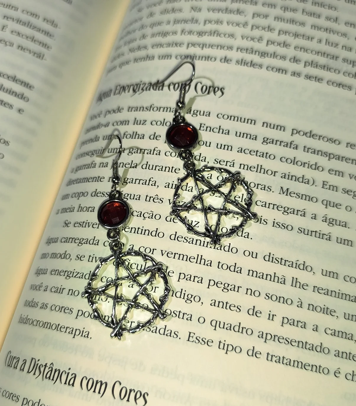 Brinco pentagrama místico vermelho gótico em liga metálica prateada texturizada sobre as páginas de um livro.