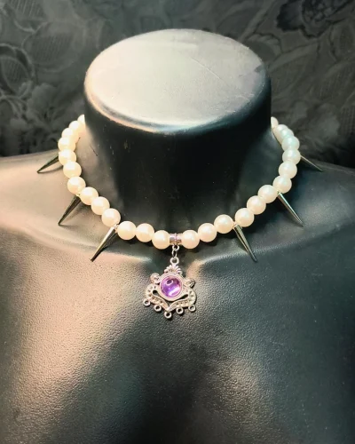 Choker com miçangas peroladas brancas com seis spikes prateados e pingente de liga metálica com pedra roxa central.
