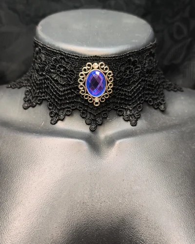 Gargantilha de renda preta trabalhada com medalhão prateado e gema azul central.