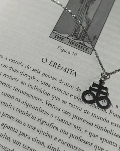 olar cruz de leviatã gótico totalmente em aço inox posicionado sobre a página do livro O Eremita.