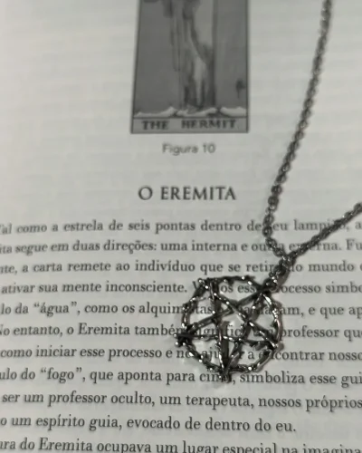 Colar pentagrama místico gótico com corrente de aço inox e pingente de liga metálica sobre a página do livro O Eremita.