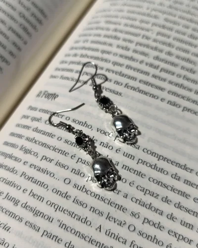 Brinco caveira gota preta gótico em liga metálica prateada com strass preto sobre as páginas de um livro.